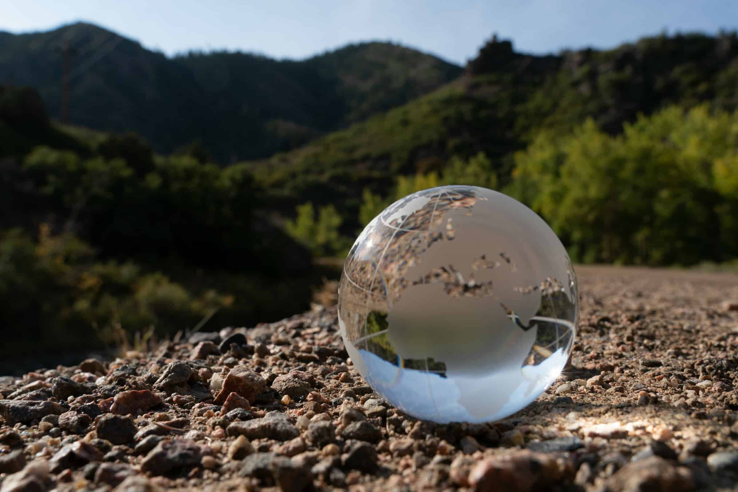 glass globe sitting on the dirt with green mountains behind